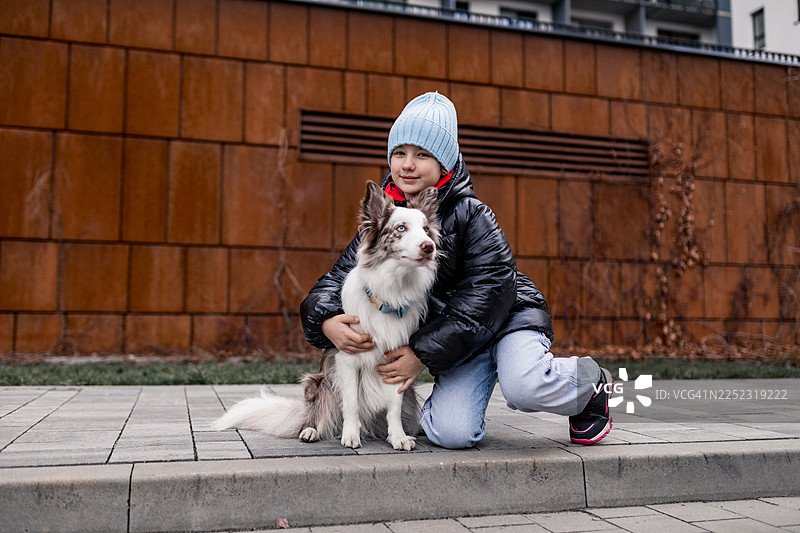 穿着冬装的小女孩在城市公园里拥抱一只友好的狗狗图片素材