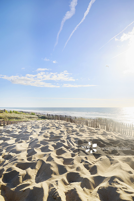 蓝天白云下，越过沙丘草地和栅栏，可以看到海滩和大海的景色图片素材