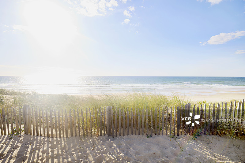 沙丘上的草和栅栏延伸至海滩和大海，背景是蓝天白云图片素材