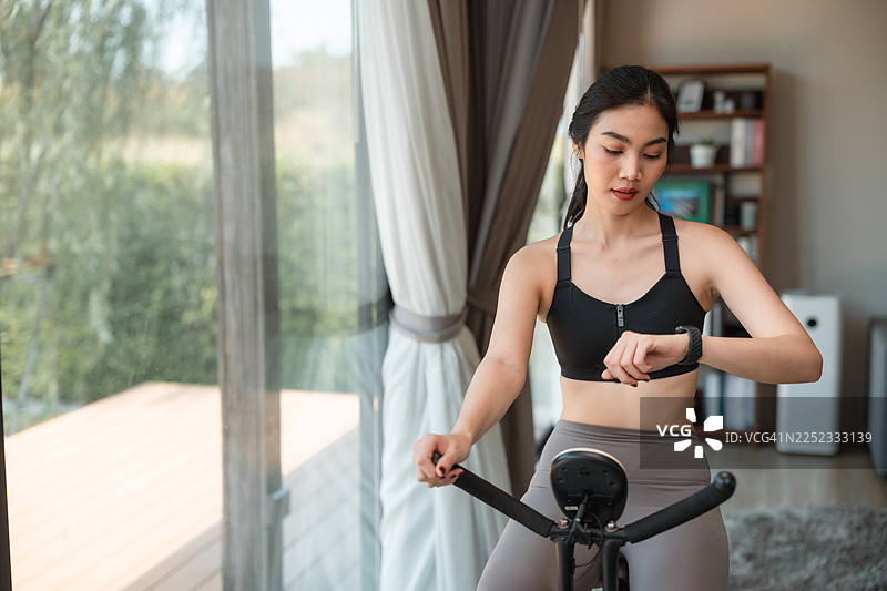 年轻女子在家运动时，在智能手表上使用骑行追踪器图片素材