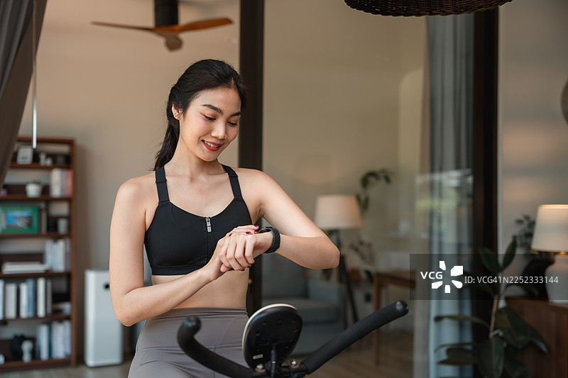 一位运动型年轻女子在家锻炼时，在智能手表上使用骑行追踪器图片素材