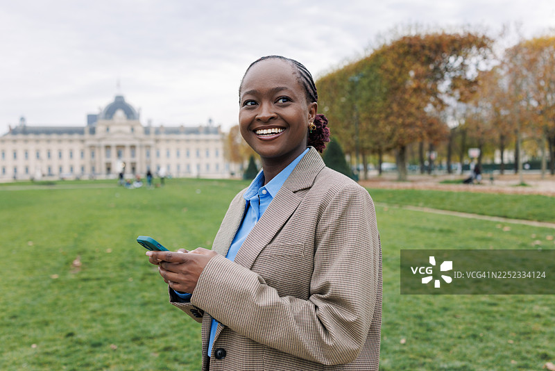 年轻女子在公园里对着手机微笑，背景是历史建筑图片素材