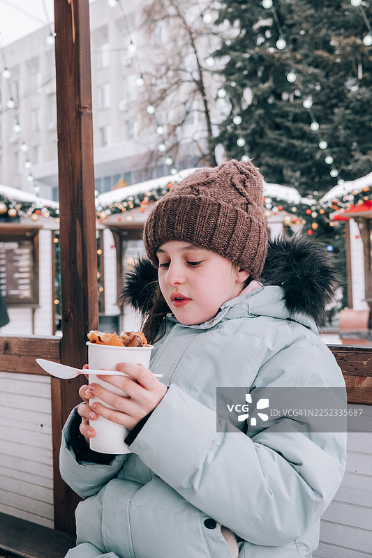 一个女孩在圣诞集市上吃甜点。图片素材