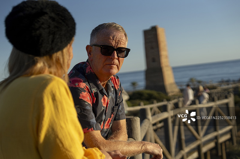 夕阳下，一对年迈夫妇在海边木栈道上的肖像照图片素材