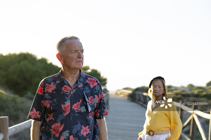 夕阳下，一对老年夫妇在海滩旁的木质走道上合影图片素材