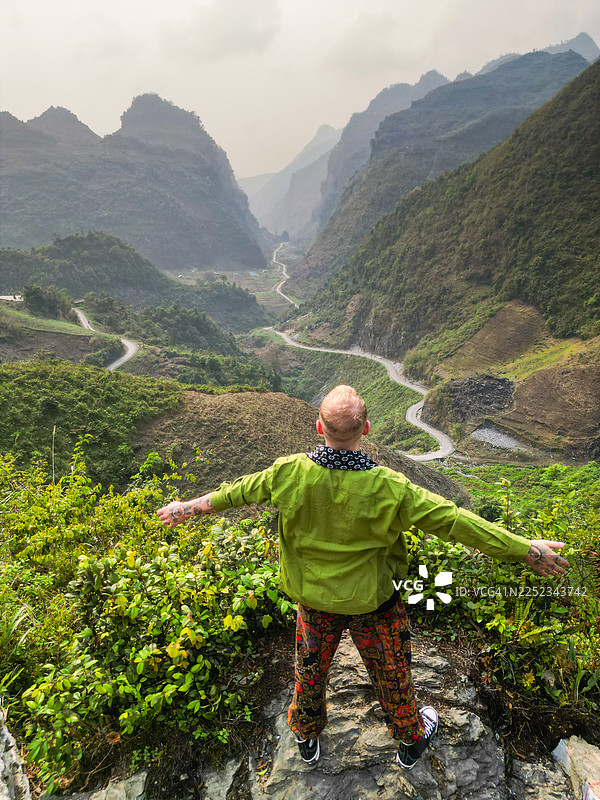 背景是河江雄伟的石灰岩和绿色山峰，前景中的年轻男子摆姿势，与令人惊叹的景色融为一体图片素材