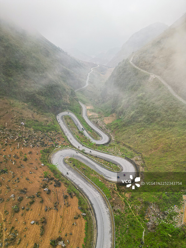高空视角俯瞰蜿蜒的河江环线公路，骑行者和摩托车穿行在陡峭的山峦之中图片素材