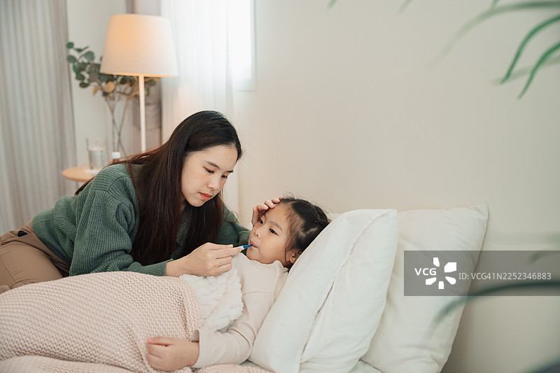 一位担忧的亚洲母亲正在给卧病在床的女儿量体温图片素材