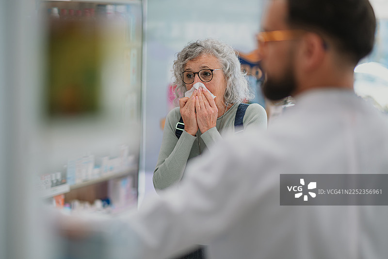 一位年长的女士在药店里擤鼻涕并寻求建议图片素材