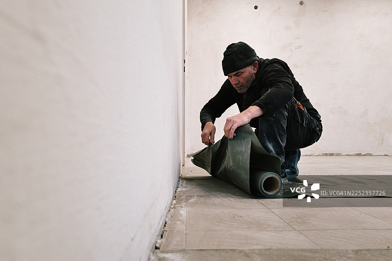 建筑工地：工人在地板上切割油漆工遮蔽膜图片素材