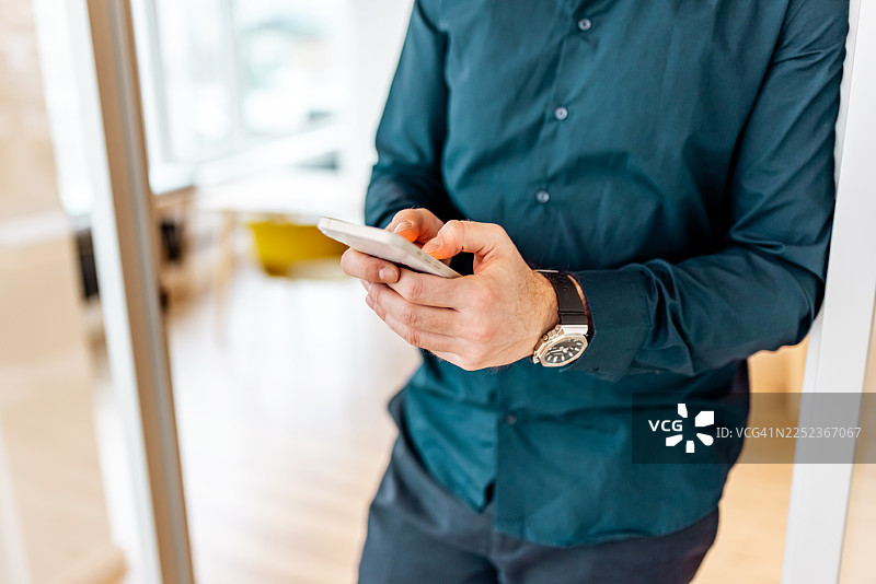一位专业男士在现代办公室使用智能手机进行商务沟通图片素材