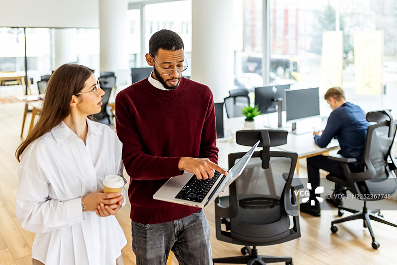 笔记本电脑、咖啡和开放式办公空间中，同事间的现代办公室协作图片素材