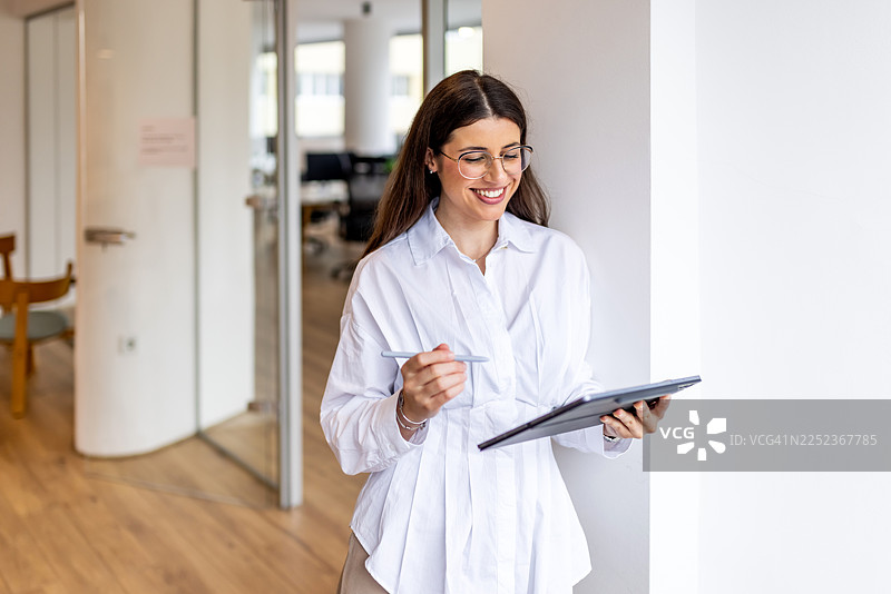 职业女性在现代办公室使用平板电脑，面带微笑地记录笔记图片素材