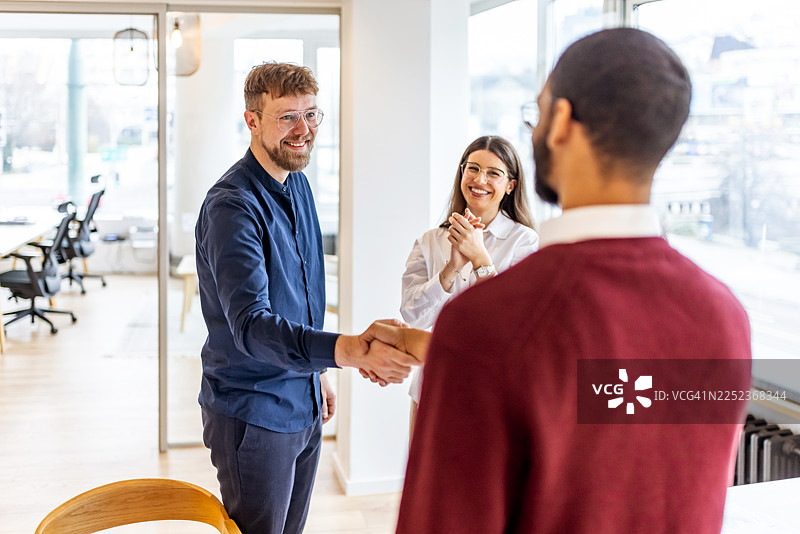 现代办公室里，同事们握手庆祝合作，脸上洋溢着笑容图片素材