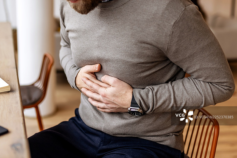 穿着休闲服的男子在室内咖啡馆内因胃部不适而捂着腹部图片素材