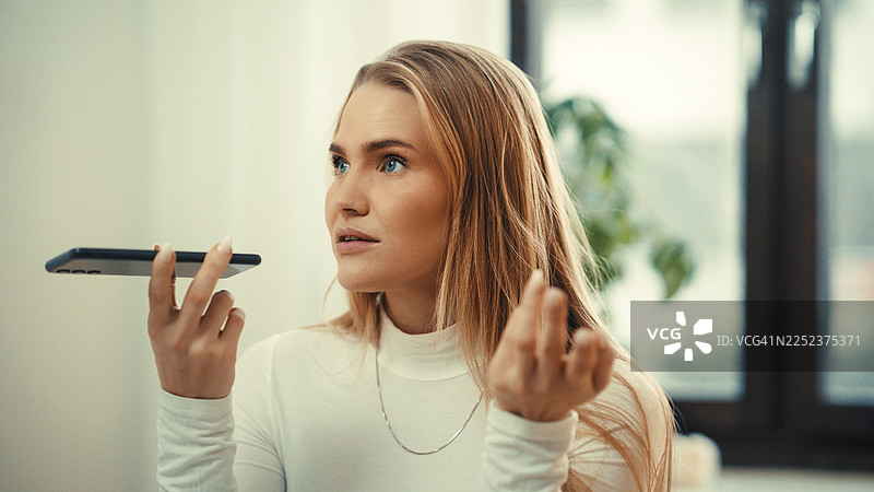 女子在家中将智能手机用作虚拟助手，专注于收听设备。图片素材