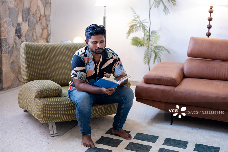 一位亚洲成年男性在沙发上静静地读着一本好书图片素材