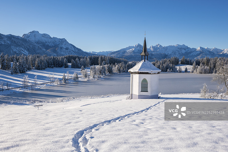 雪景，有小教堂和脚印，背景是山脉，位于德国巴伐利亚州阿尔高地区福森附近的赫格拉茨里德湖畔图片素材