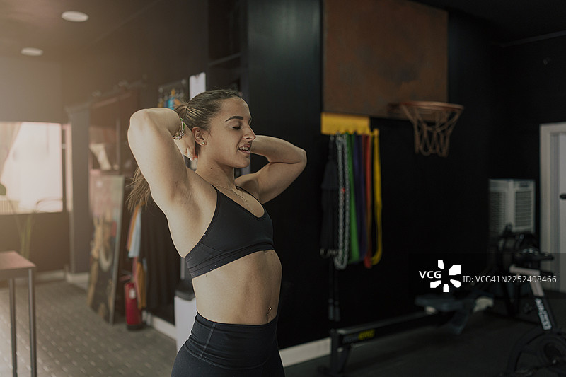 年轻女子在健身房伸展手臂，头在脑后图片素材