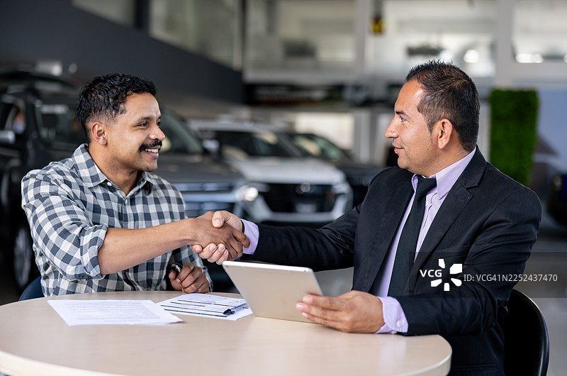 一位快乐的男士在经销商处购车后与销售人员握手图片素材