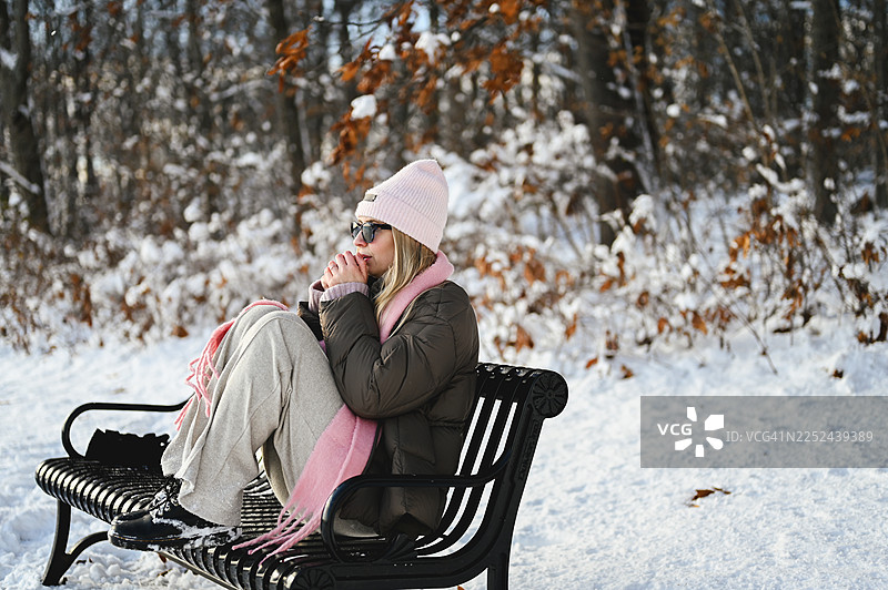 年轻女子冬天坐在公园长椅上图片素材