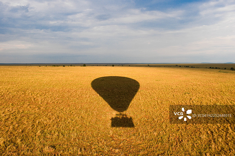 热气球的影子投射在非洲草原多云天空下的金色草地上图片素材