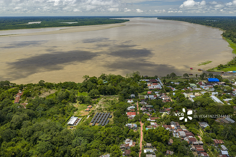 俯瞰图：一片社区依偎在宽阔的河流旁，周围环绕着郁郁葱葱的绿色雨林，天空布满云彩。图片素材