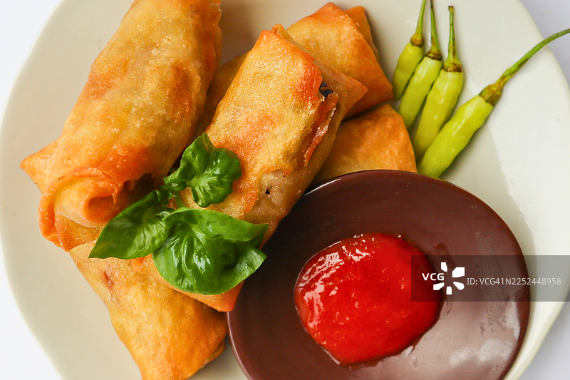 俯视角度拍摄的美味春卷，配有辣椒和蘸酱，盛放在白盘中图片素材