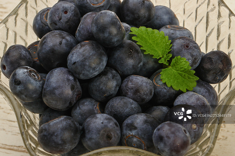 高角度拍摄的玻璃碗内新鲜蓝莓与薄荷叶，背景为木质图片素材