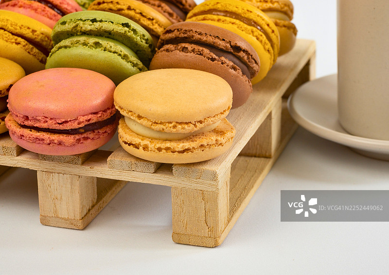 色彩缤纷的法式马卡龙摆放在小木托盘上，旁边放着一杯，展示了多种口味和令人愉悦的甜点图片素材