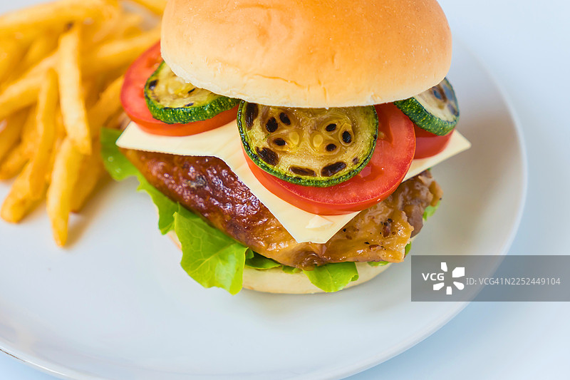 白色盘子盛着的美味烤鸡肉汉堡，配有新鲜蔬菜和奶酪，旁边是香脆的炸薯条图片素材