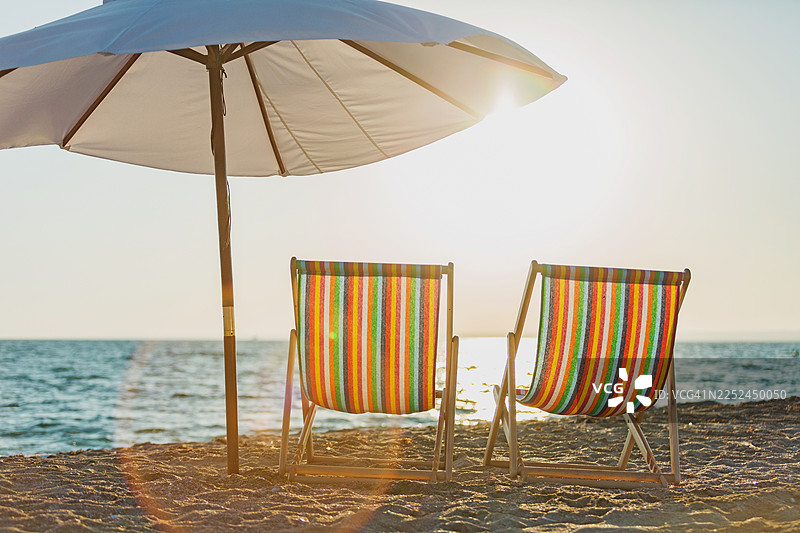 日落时分，沙滩上放置着两把空荡荡的彩色躺椅，旁边有一个遮阳伞，背景是海洋，印度尼西亚图片素材