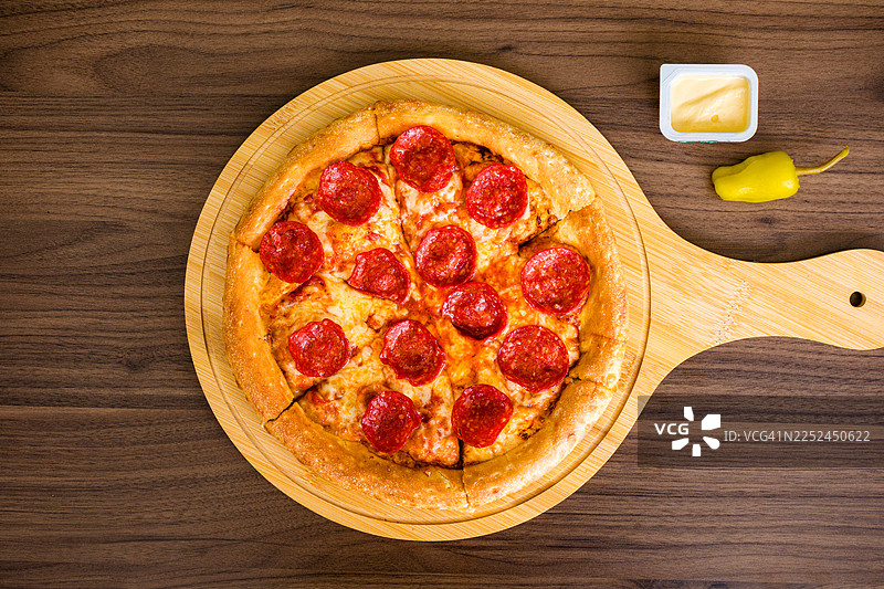 一个装有辣香肠披萨的木制托盘，配有蘸酱和意大利辣椒，俯视角度拍摄图片素材