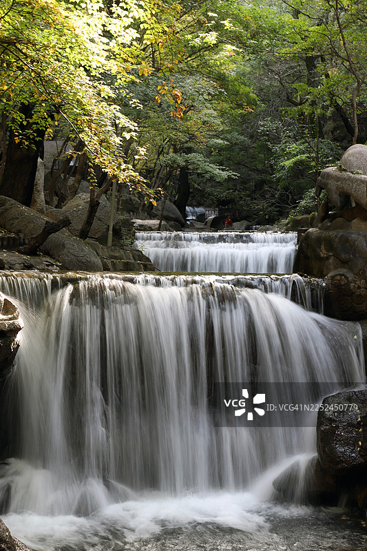 中国，阳光穿透树林，郁郁葱葱的绿色森林中，多层瀑布倾泻而下的风景图片素材