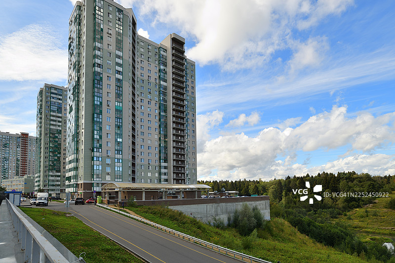 明亮的阴天，现代住宅楼矗立在繁茂的绿色景观之上，一条道路通向城市。图片素材