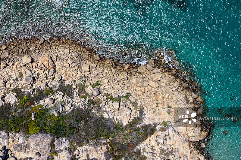 从空中俯瞰崎岖的海岸线，碧绿的海水拍打着岩石海岸，岸边点缀着翠绿的植被图片素材