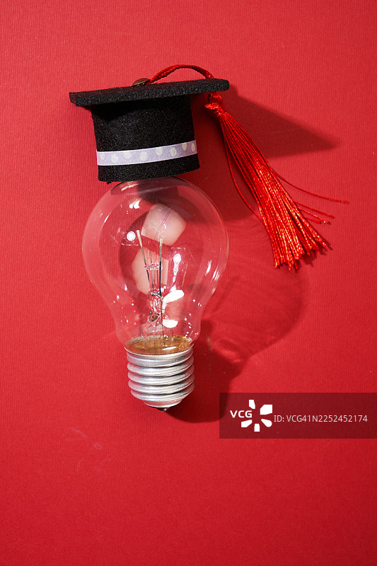 带有毕业帽的灯泡，象征着红色背景上的想法或教育图片素材