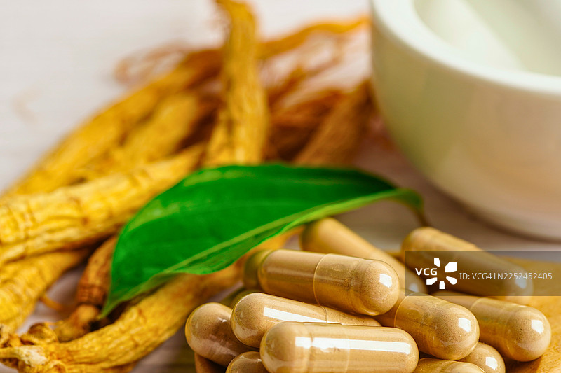 特写镜头，画面为木桌上的天然草本胶囊，配以人参根和研杵研钵，强调健康与养生。图片素材