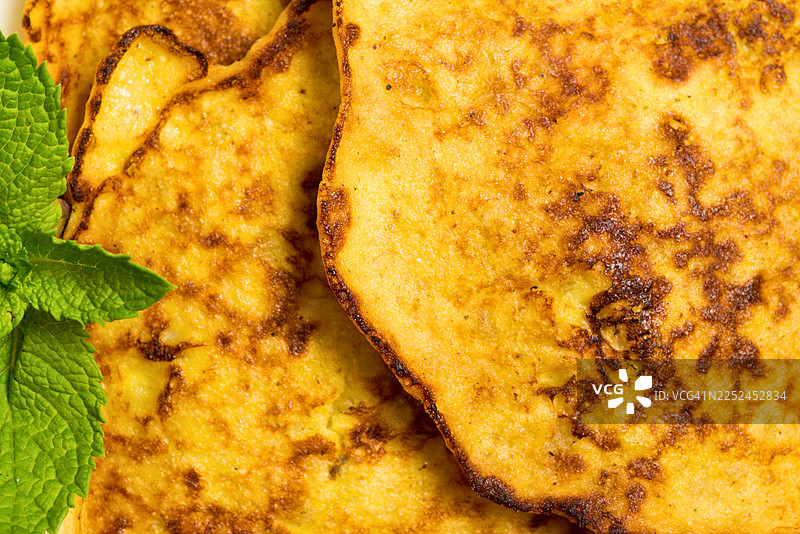 金黄酥脆的煎饼特写，配以新鲜的薄荷叶，是美味的早餐或点心图片素材