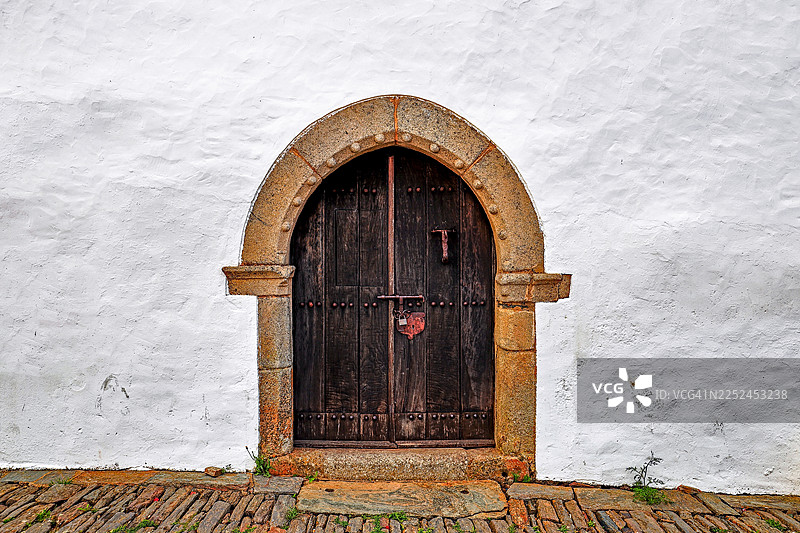 白色灰泥墙上的石头拱门旁带有乡村风格的木门，唤起了历史建筑的记忆，葡萄牙蒙萨拉斯图片素材