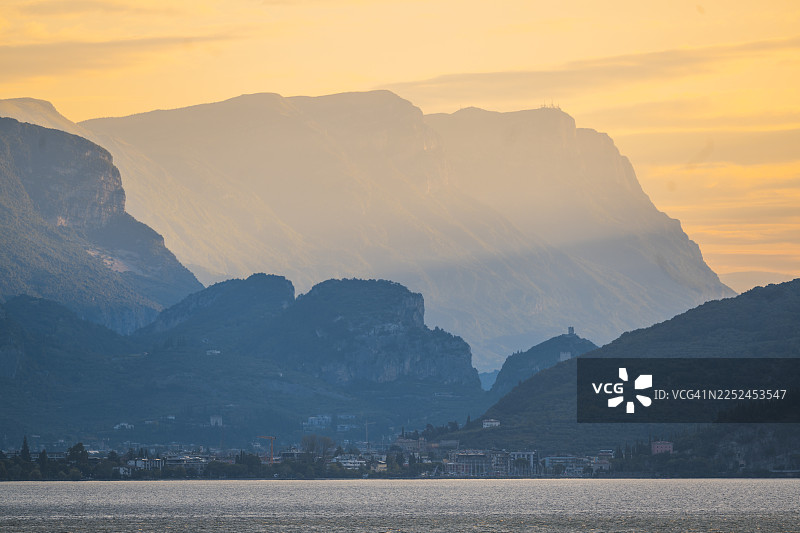 意大利加尔达湖畔，夕阳映照着宁静的湖面和高耸的山峦图片素材