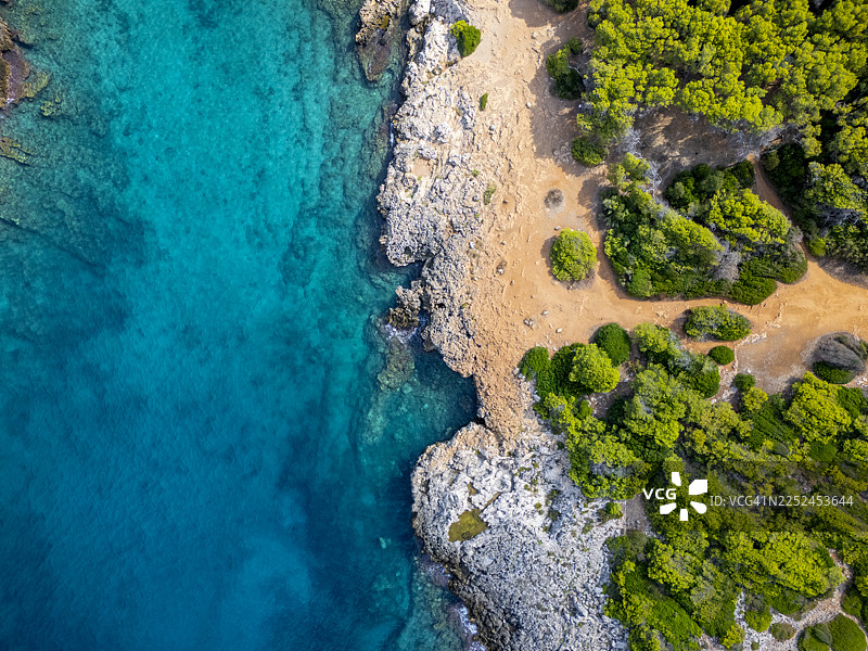 从空中俯瞰，碧绿的海水与岩石海岸线和沙滩交汇，四周环绕着郁郁葱葱的绿树，普利亚地区图片素材