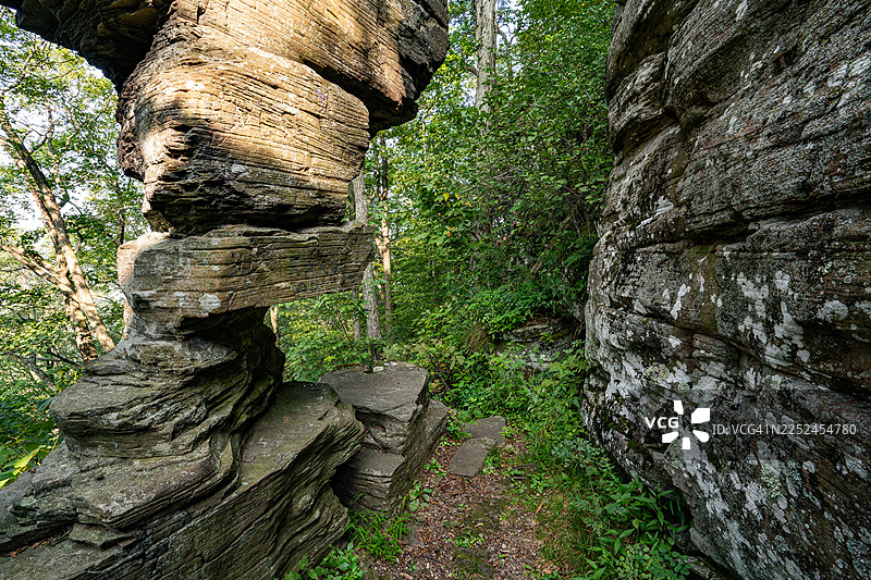 古老的岩石构造巍然屹立于茂密的绿色森林之中，在一条远足小径上形成天然的入口，美国，美国，苏利文县图片素材