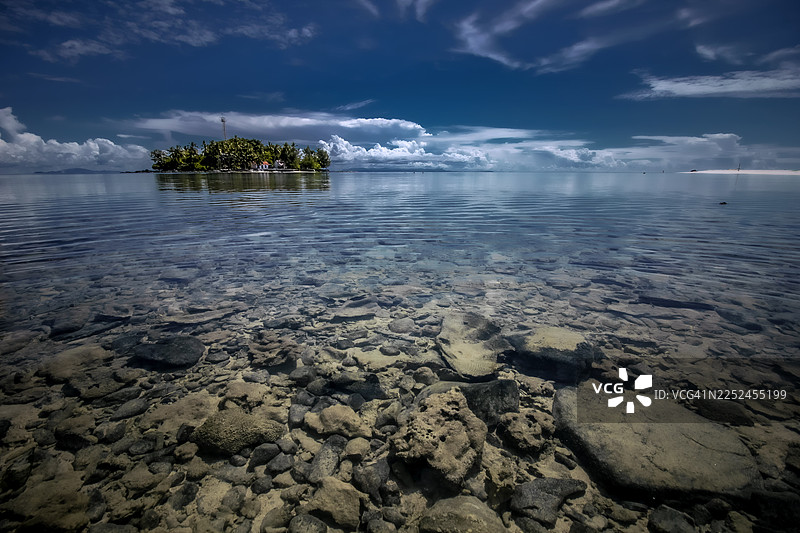 热带天堂岛屿，拥有清澈的蓝色海洋和岩石海底，天空戏剧般地变化着。图片素材