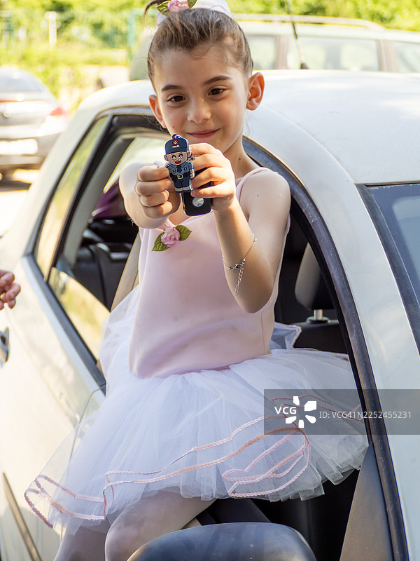 身穿芭蕾舞裙的女孩坐在车里，手里拿着警车玩具钥匙图片素材