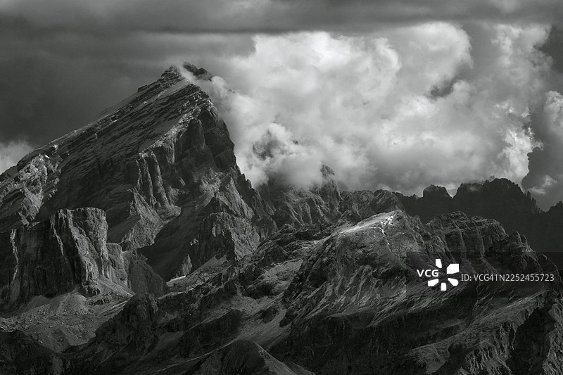崎岖的雪山在多云的天空下，薄雾缭绕山峰，戏剧性的黑白风景照。图片素材
