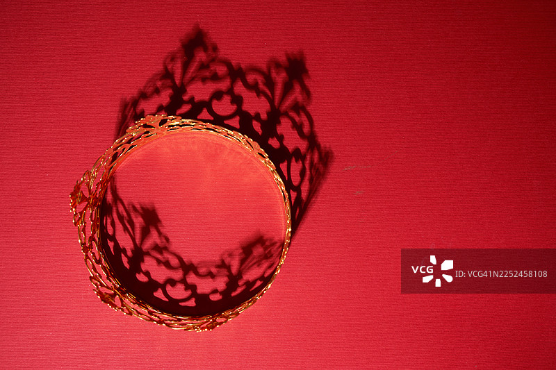 金色皇冠在红色织物上投下精致的阴影图片素材