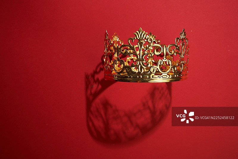 鲜艳的红色背景上有一顶金色皇冠，投下戏剧性的阴影图片素材