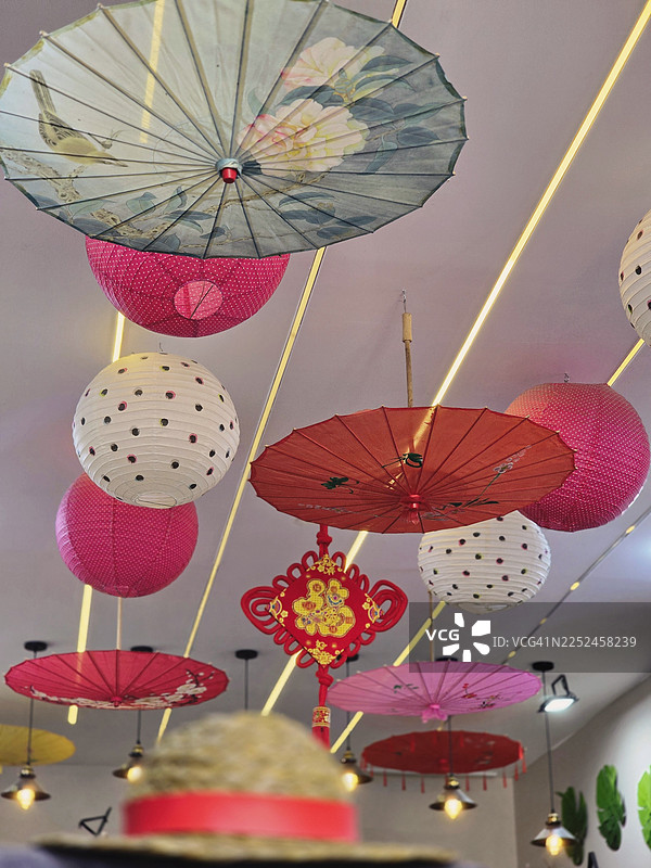 色彩鲜艳的亚洲风格灯笼和纸伞悬挂在天花板上，营造出喜庆而富有装饰性的氛围图片素材