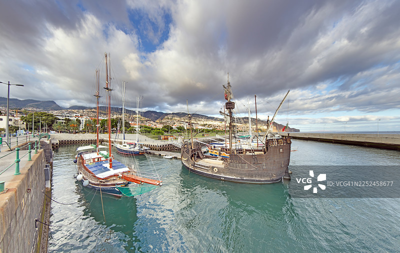 葡萄牙马德拉群岛，丰沙尔港，历史悠久的船只和现代船只停靠在戏剧性的天空下图片素材